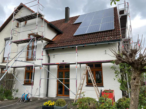Eingerüstetes Wohnhaus mit Photovoltaikanlage während des Anstrichs