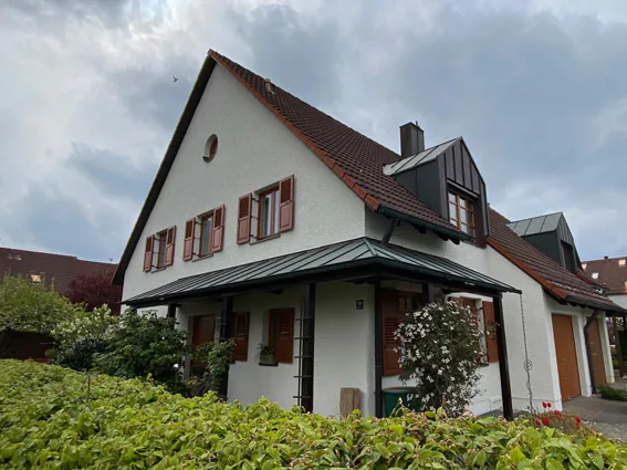 Weißes Landhaus mit rot abgesetzten Fensterläden und grünem Vordach