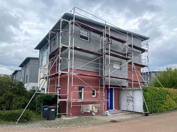 Mehrfamilienhaus im Gerüst mit rot abgesetzter Fassade
