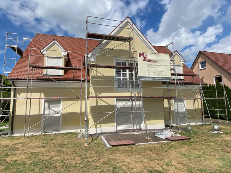 Einfamilienhaus im Gerüst während des Fassadenanstrichs, die neue Farbe ist bereits zur Hälfte aufgetragen