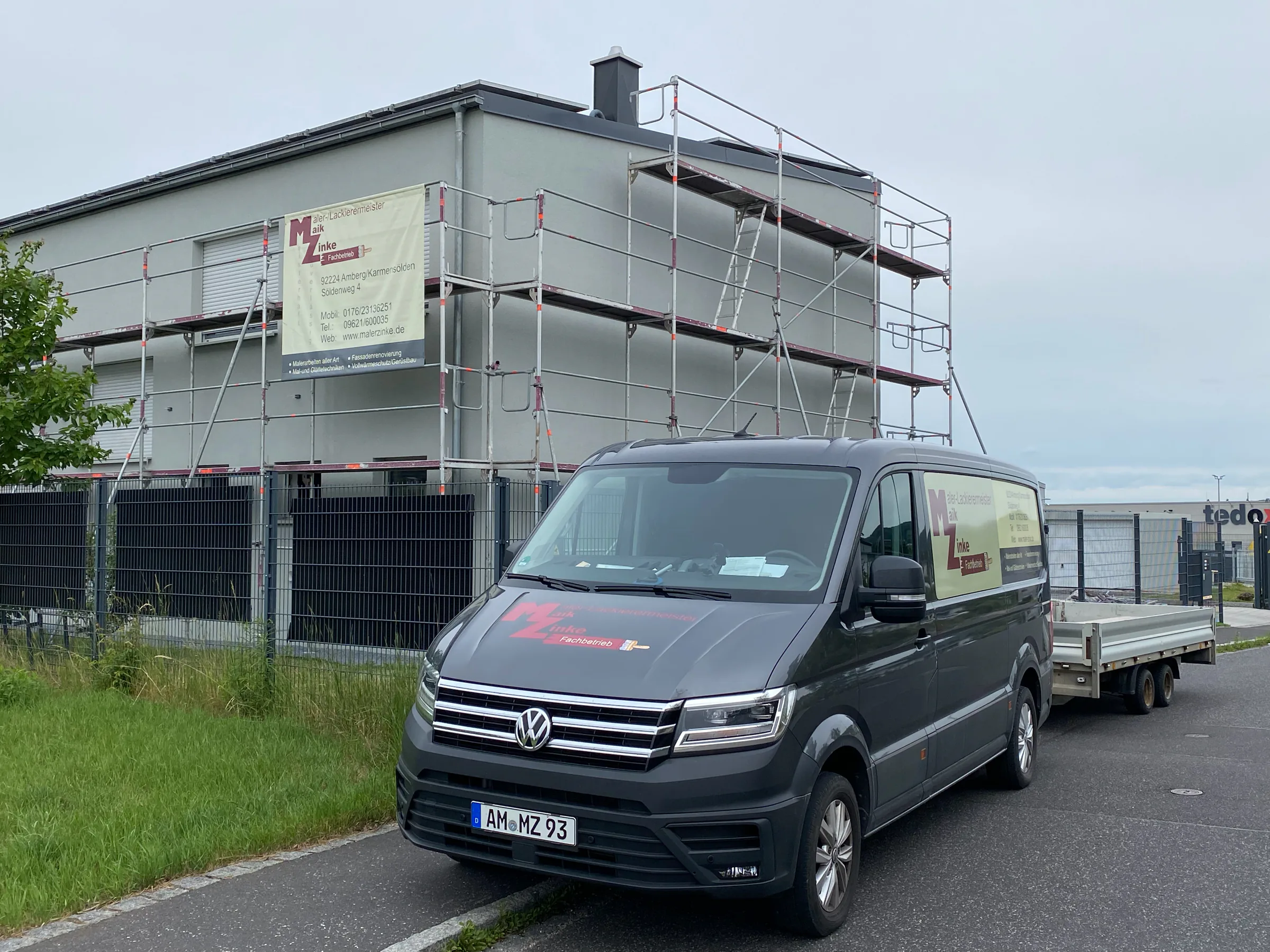 Nahansicht des eingerüsteten Gewerbebaus mit Firmenwagen und Materialanhänger