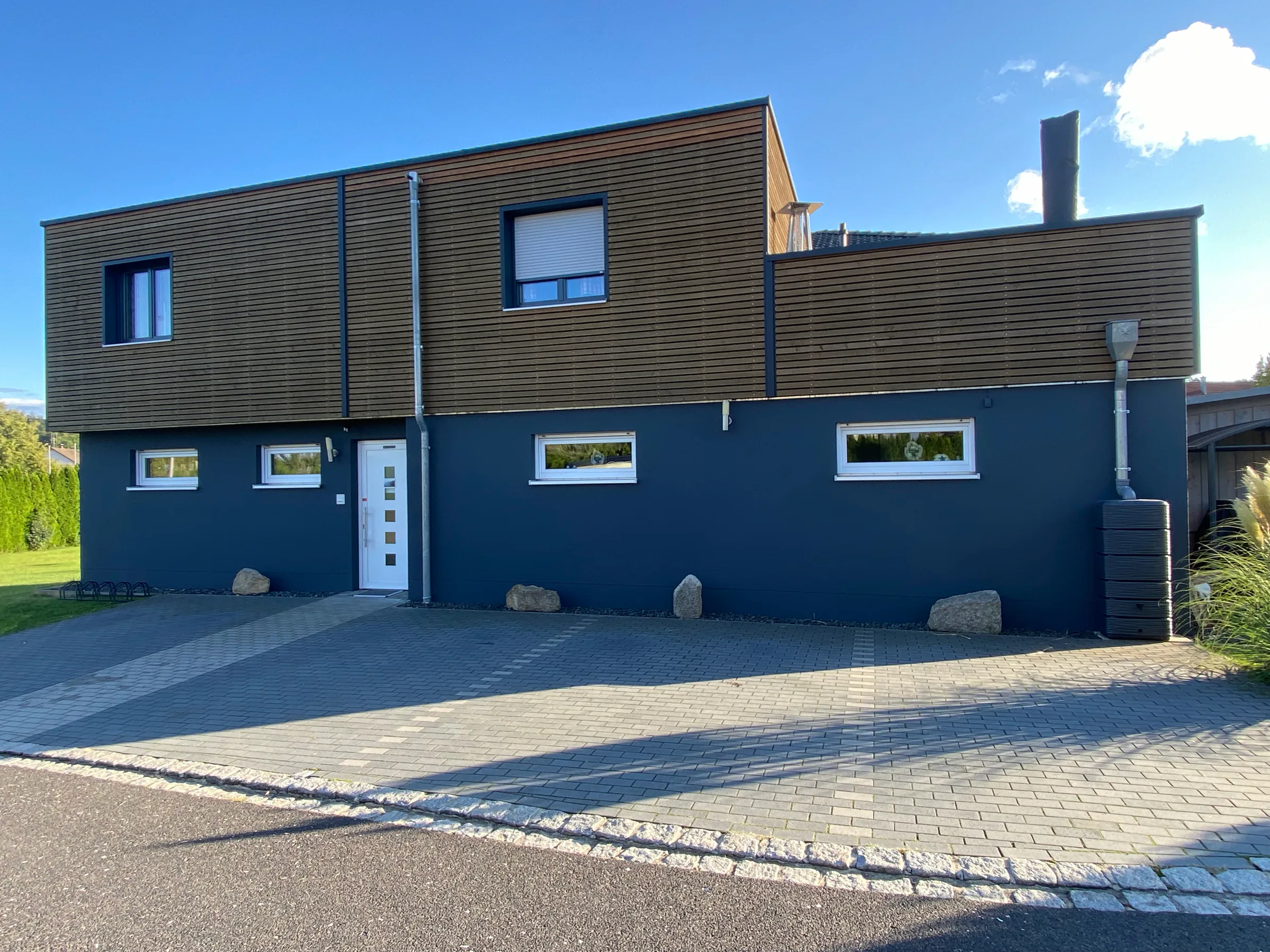 Modernes Wohnhaus mit dunkel gestrichenem Erdgeschoss und Holzverschalung im Obergeschoss vor tiefblauem Himmel